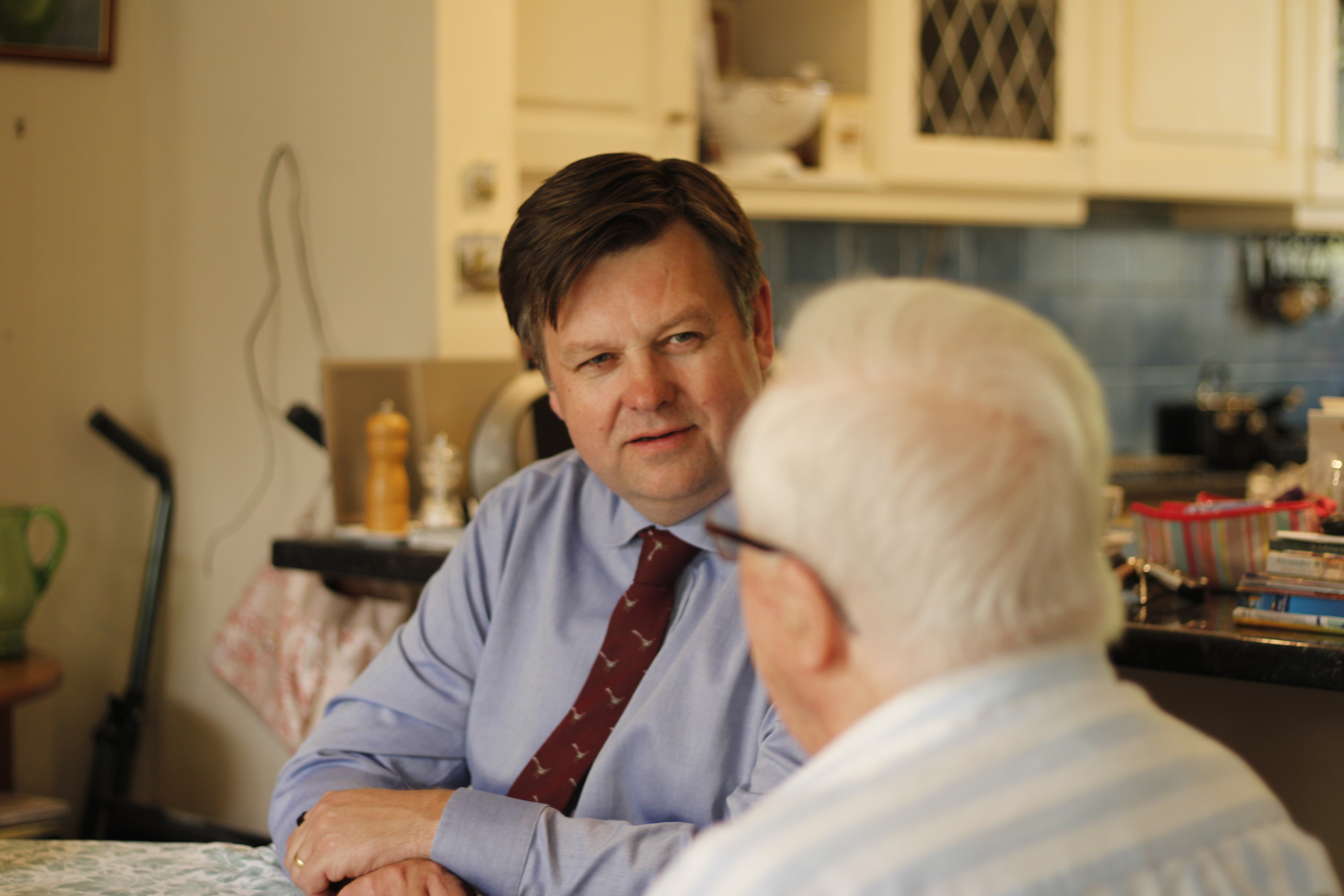 Andrew Baxter sat at a table talking with an older person.